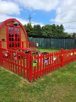 a red fence with a small house in a yard at Glamping Pod in St Austell Sleeps 2 with Spa Pool in St Austell
