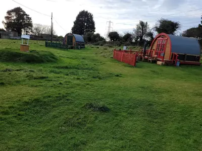 a field with two tents and a red fence at Cozy Cabin Retreat in Saint Austell in Lanivet