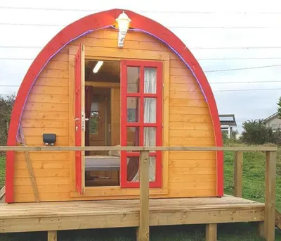 a large wooden cabin with a red door on a deck at Cozy Cabin Retreat in Saint Austell in Lanivet