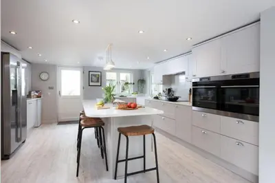 a kitchen with white cabinets and a white island with stools at Beach Cottage and The Lobster Pot in St. Agnes