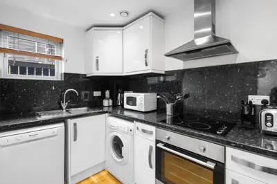 a kitchen with white cabinets and a washer and dryer at Silvercroft Cottage - Luxury Modern Coastal Retreat Near Beach, Sleeps 4 in Porthtowan