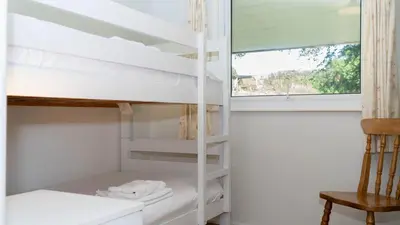 a room with bunk beds with a window and a chair at Ta Mill Cottages & Lodges - Meadowview Chalet 4 in Launceston