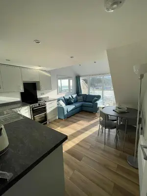 a kitchen and living room with a couch and a table at Whispering Waves in Porthtowan, Beachfront Apartment in Porthtowan