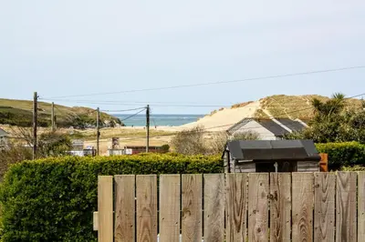 a wooden fence with the ocean in the background at Pollymoor Beach House in Holywell Bay