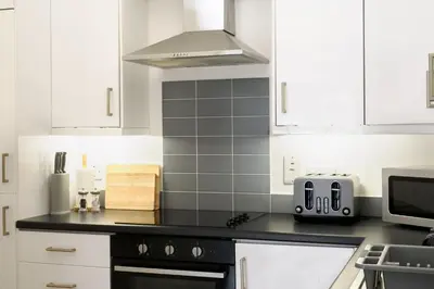 a kitchen with white cabinets and a black counter top at Sennen in Budock Water