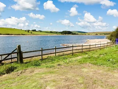 a fence next to a body of water with a beach at Higher Kernick View in Bodmin