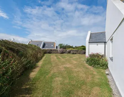 a yard with a white house and a fence at Kirra in Polzeath