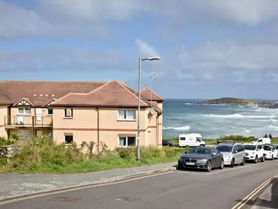 a street with cars parked next to a house and the ocean at Apartment 1 Waterrs Edge in Crantock