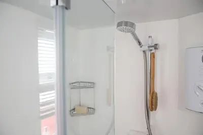 a shower in a white bathroom with a shower head at Stunning Sea Views, Wi-Fi, Pet Friendly in Marazion