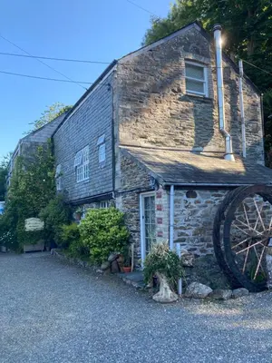 an old stone house with a large wheel in front of it at Bissick Old Mill Suite in Truro