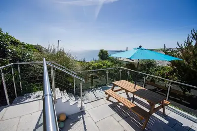 a patio with a bench and an umbrella at Coastguard Cottage Cornwall - Sea & Harbour Views in Mevagissey
