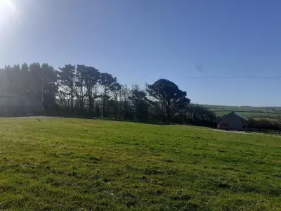 a green field with trees and a barn in the distance at Hawk's Nest in Wadebridge