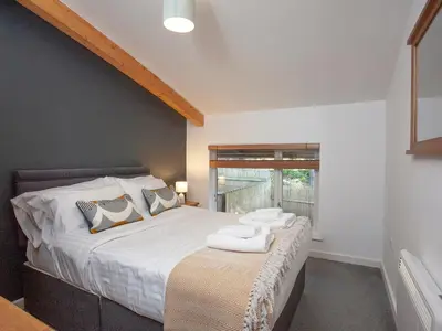 a bedroom with a bed with white sheets and a window at Trebisken - Cottage in Porthtowan