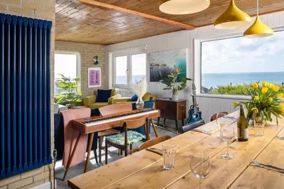 a dining room with a table and a piano at Sunset Beach House Porthleven in Porthleven