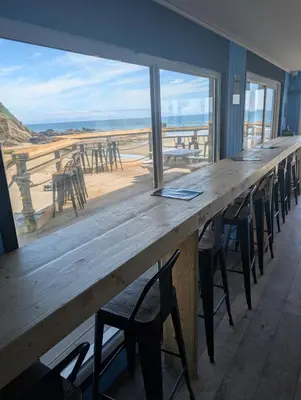 a long wooden table with chairs and a view of the beach at May View - Luxury Sea View Apartment - Millendreath, Looe in Looe