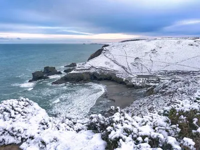 a snow covered cliff with a beach and the ocean at Chy Cos. South facing lodge with balcony & views. in St. Agnes