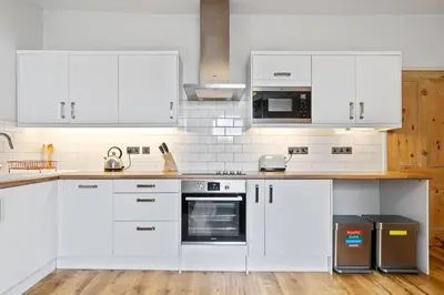 a white kitchen with white appliances and wooden floors at Pendennis - Bright Victorian flat, sea views & close to beach in Falmouth