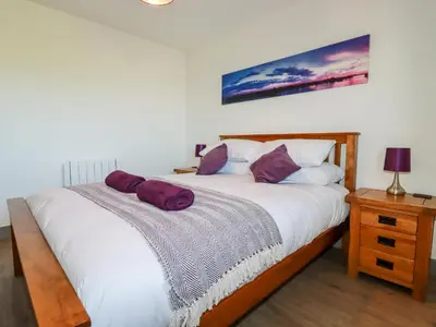 a bedroom with a large white bed with purple pillows at Bimbling Cottage in Redruth