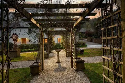a wooden pergola with a table in a garden at Linhay at East Trenean Farm -Luxury retreat for 2 with stunning rural views, private hot tub and EV charging in Looe
