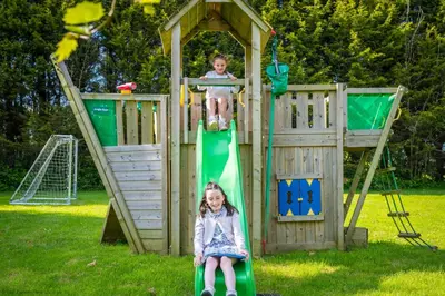 two children playing on a playground with a slide at Corn Barn at East Trenean Farm -Luxury Cornish Barn Conversion sleeping 8 with hot tub, private garden, rural views and EV facilities in Looe