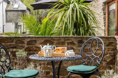 a table with a tea set on it with two chairs at Water Mill at East Trenean Farm -Luxury Cornish Cottage sleeping 4 with hot tub, private garden, rural views and EV facilities in East Looe