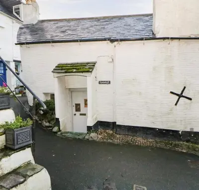 a white building with a garage with a cross on it at SPINDRIFT is A Beautiful Newly Refurbished THREE BEDROOM Private Family House located on the OLD HARBOUR and the COASTAL PATH in the Heart of Beautiful POLPERRO in Polperro