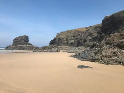 a sandy beach with rocks and the ocean at Tides Reach, Deluxe Shepherds hut 1, 100m from the Beach in St Merryn