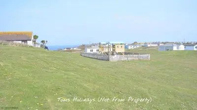 a grassy field with houses on the side of a hill at F62 Near Sea, Riviere Towans in Hayle