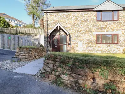 a brick house with a brown door and a stone wall at Brewers Cottage in Looe