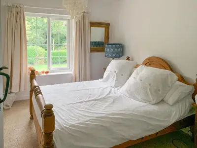 a bedroom with a bed with white sheets and a window at Castle Cottage in Ruan Lanihorne